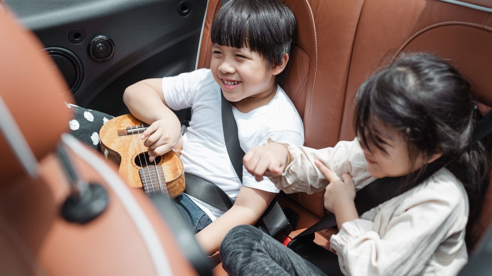 Two children buckled up and laughing together in a car back seat